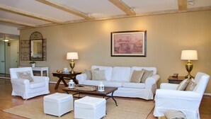 A living room with a white sofa set, two side tables with lamps, a coffee table, and a framed cityscape painting on the wall.