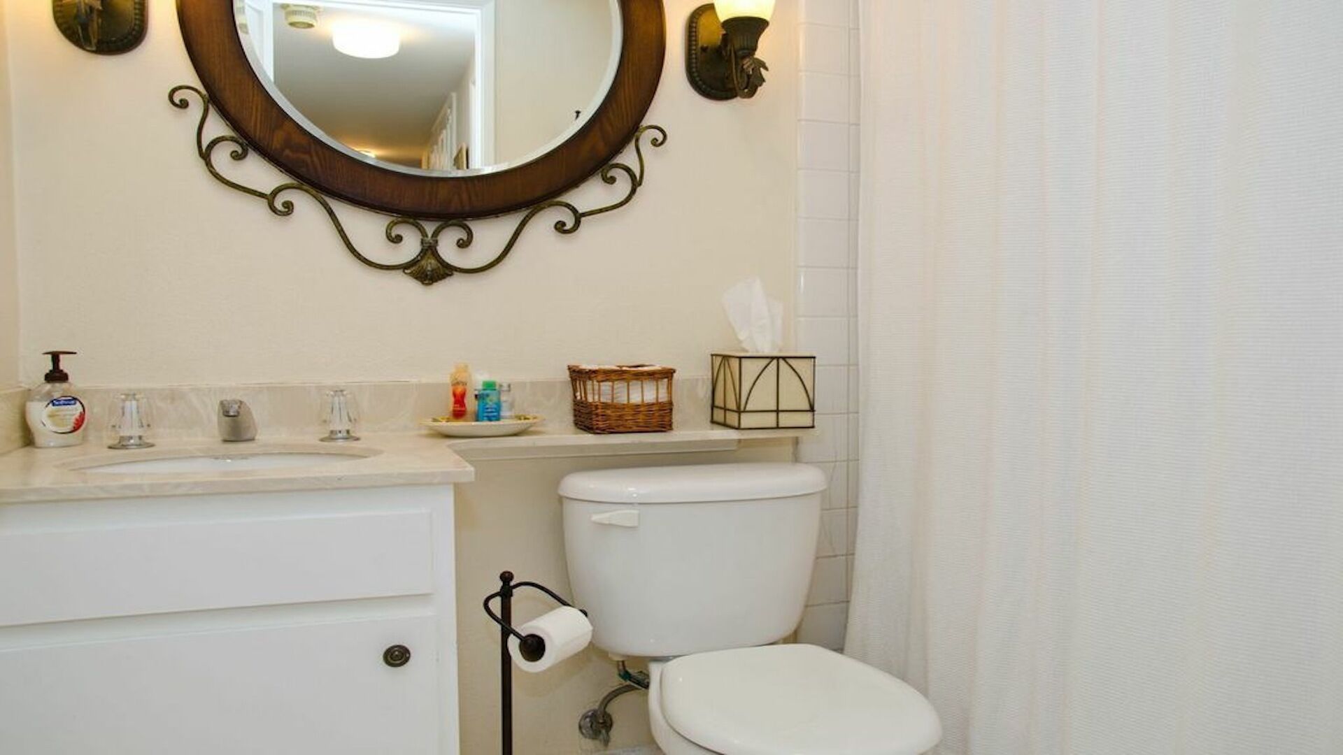 A bathroom with a white toilet, a sink with a mirror above it, and a basket of toiletries on the counter.