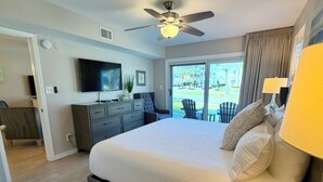 A bedroom with a bed, a ceiling fan, a TV, a dresser, and a view of the outdoors.