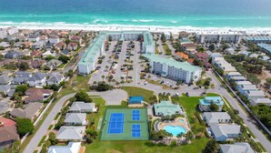 An aerial view of a coastal hotel with multiple buildings, a parking lot, and a beach in the background.