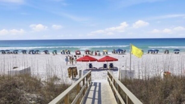 A beach with a wooden walkway leading to the water, umbrellas, and beachgoers.