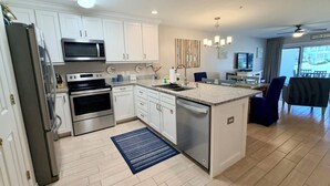 A modern kitchen with white cabinets, stainless steel appliances, a central island, and a dining area with chairs.
