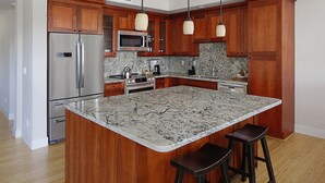 Una cocina con armarios de madera, electrodomésticos de acero inoxidable, encimera de mármol e iluminación colgante.