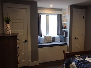A bedroom with a window seat, a dresser, and a bed.