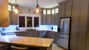 A modern kitchen with granite countertops, stainless steel appliances, and a central island with bar stools. - Picturesque oceanfront / beachfront estate, PEI tourism license # 2101170 (Burton)