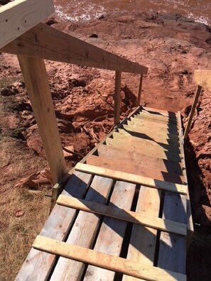 A wooden deck with a sloped design, supported by wooden posts, set on a sandy terrain.