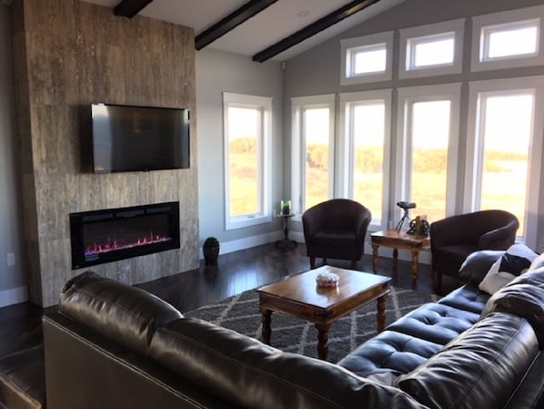 A spacious living room with a fireplace, leather sofas, and large windows offering a view of the outdoors.