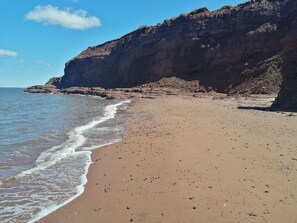 A beach with a rocky cliff and calm waves.