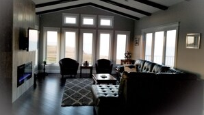 A spacious living room with a high ceiling, large windows, a fireplace, and a leather sofa. - Picturesque oceanfront / beachfront estate, PEI tourism license # 2101170 (Burton)