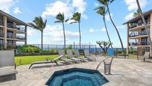 A pool area with lounge chairs, a hot tub, and a view of the ocean.