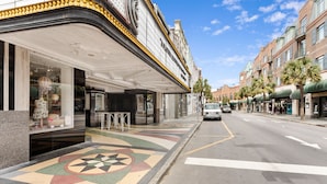 A street with a theater building, a sidewalk with a colorful mosaic, and a clear blue sky.