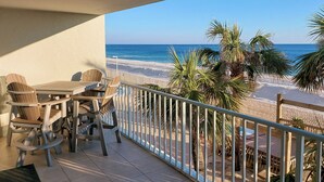 Un balcone con vista sulla spiaggia, un tavolo e sedie, e una ringhiera.