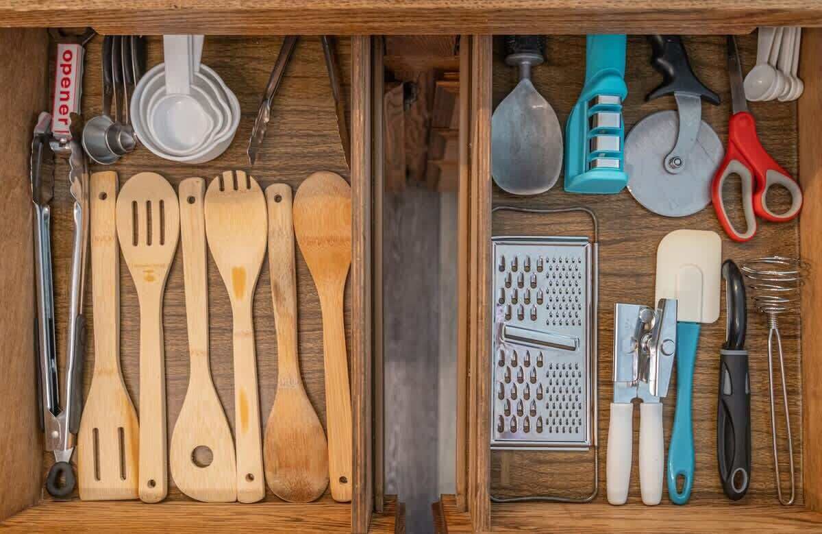 A drawer with wooden utensils, a grater, and various kitchen tools.
