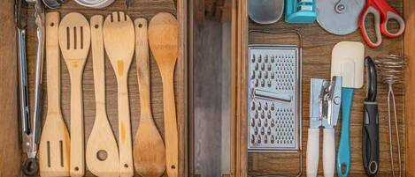 A drawer with wooden utensils, a grater, and various kitchen tools.