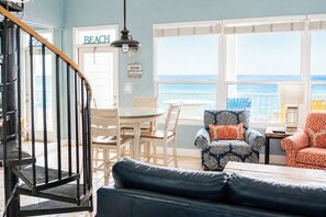 A room with a dining table, chairs, a blue patterned armchair, a blue sofa, and a view of the ocean through large windows. - BLUE DOLPHIN PENTHOUSE LUXURY 3 BDR 3 BA 2026 Booking Fast (Fort Walton Beach)
