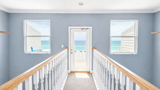 Una scala con balaustre bianche e corrimano in legno che conduce a una porta con vista sull'oceano.