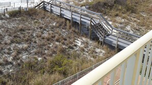 Vista sulla spiaggia con una passerella in legno che conduce a una spiaggia sabbiosa, una piscina e un cielo azzurro limpido.