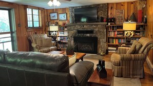 A living room with a fireplace, a television, a ceiling fan, and a bookshelf. - Waterstone Cottage - Outdoor Fireplace, Serene Pond, Rocking Chair Front Porch (Canton)