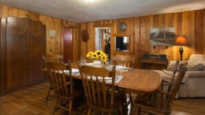 A wooden-paneled room with a dining table set for four, surrounded by wooden chairs. - Waterstone Cottage - Outdoor Fireplace, Serene Pond, Rocking Chair Front Porch (Canton)