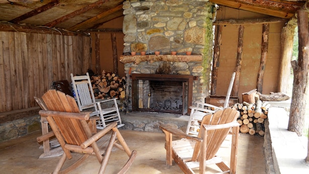 A rustic interior with a stone fireplace, wooden chairs, and a log stack. - Waterstone Cottage - Outdoor Fireplace, Serene Pond, Rocking Chair Front Porch (Canton)