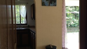A hallway with a kitchen area, a trash bin, and a door leading to an outdoor area. - A charming house surrounded by beautiful nature. Cosy, WiFi & fully equipped. (Nuevo Arenal)