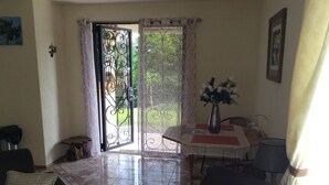 A living room with a sofa, a dining table with a vase, and a door leading outside. - A charming house surrounded by beautiful nature. Cosy, WiFi & fully equipped. (Nuevo Arenal)