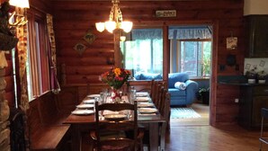 Una sala da pranzo in legno con un lungo tavolo apparecchiato per quattro persone, un lampadario e un cartello con scritto "Hut's Ale House".