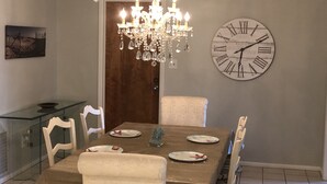 Ein Esszimmer mit Holztisch, weißen Stühlen, einer Chandelierleuchtre und einer Wanduhr.