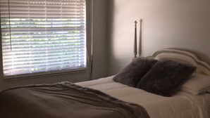 Ein Schlafzimmer mit einem Bett, einem Fenster mit Jalousien und einem Nachttisch mit Lampe.