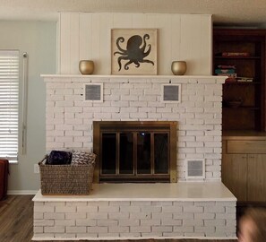 Cozy fireplace features a decorative octopus artwork and two vases, accompanied by a wicker basket and a cabinet with books and a bowl.