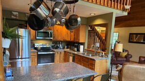 A kitchen with granite countertops, stainless steel appliances, and hanging pots. - Riverfront Chalet with Spectacular View in Cascade Mountains of Stevens Pass (Gold Bar)