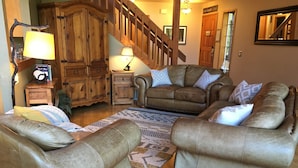 A cozy living room with leather sofas, a wooden cabinet, and a staircase. - Riverfront Chalet with Spectacular View in Cascade Mountains of Stevens Pass (Gold Bar)