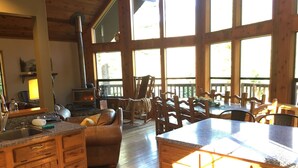 A spacious kitchen with wooden cabinets, a stone countertop, and a large island. There is a fireplace, a dining area with wooden chairs, and large windows allowing natural light. - Riverfront Chalet with Spectacular View in Cascade Mountains of Stevens Pass (Gold Bar)