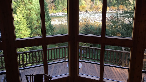 A wooden cabin with a balcony overlooking a forested area and a river. - Riverfront Chalet with Spectacular View in Cascade Mountains of Stevens Pass (Gold Bar)