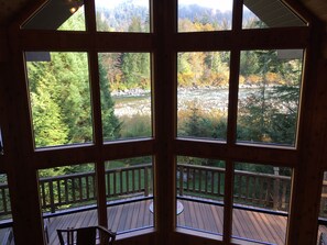 Une cabane en bois dotée d’un balcon donnant sur une zone boisée et une rivière.