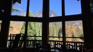 A room with large windows offering a view of a mountainous landscape and autumn foliage. - Riverfront Chalet with Spectacular View in Cascade Mountains of Stevens Pass (Gold Bar)