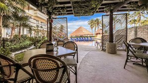 An outdoor dining area with tables and chairs, a pool with lounge chairs, and a view of a building with a thatched roof. - Ixchel Beach Hotel. Steps away from North Beach (Isla Mujeres)