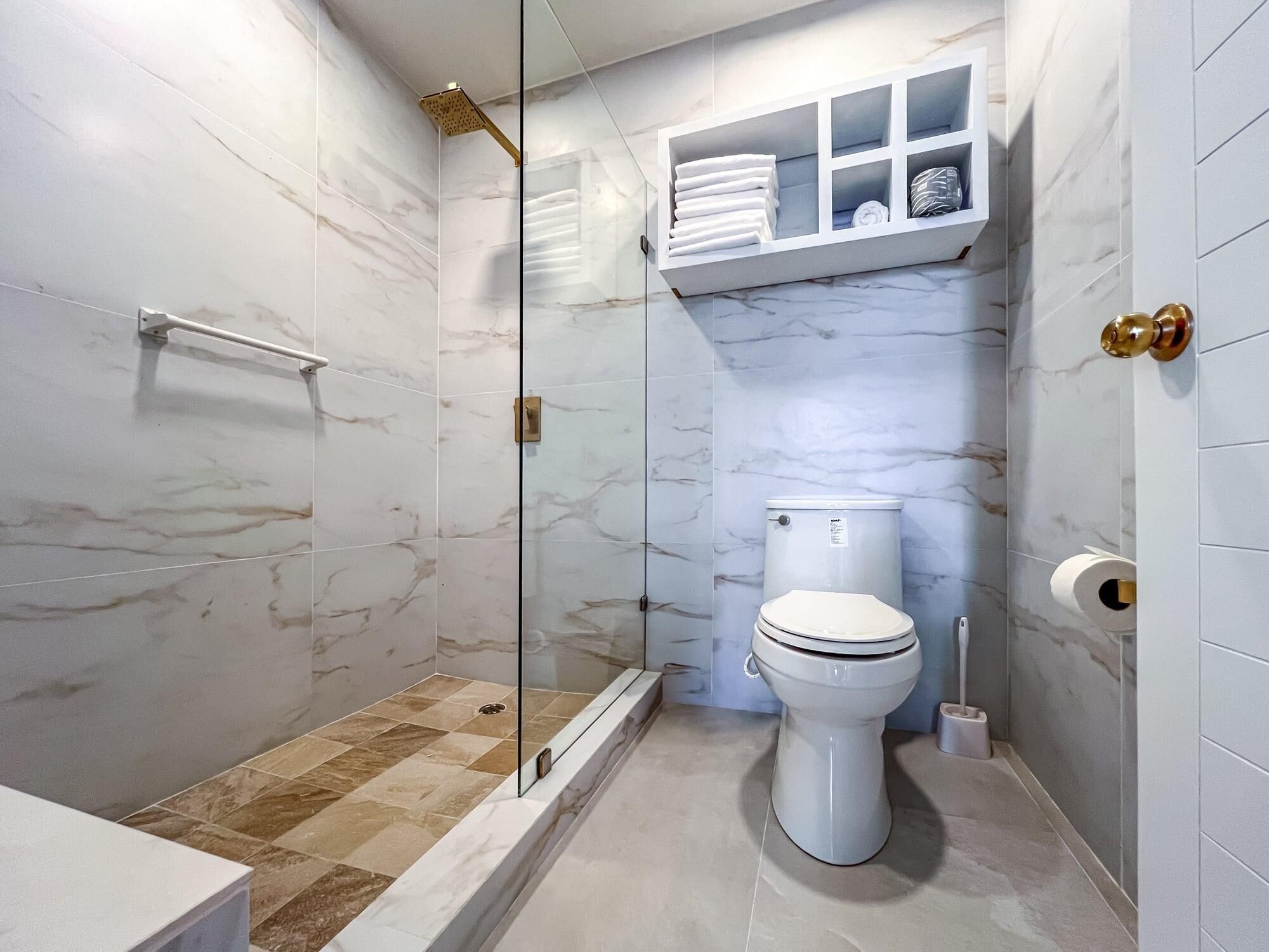 A modern bathroom with a glass-enclosed shower, a toilet, and a built-in shelf with towels.
