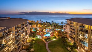 A resort with multiple floors, a swimming pool, and a view of the ocean at sunset.
