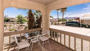 A covered patio with a table and chairs, overlooking a parking area and a desert landscape. - Incredibly Spacious Floorplan with Pool- 3 Bedroom/2 Bath Home (Lake Havasu City)