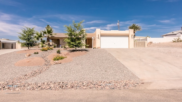 A single-story house with a garage, surrounded by a landscaped garden with small trees and shrubs. - Incredibly Spacious Floorplan with Pool- 3 Bedroom/2 Bath Home (Lake Havasu City)