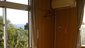 Una habitación con esteras tatami, puerta corredera de vidrio, paredes de madera y un equipo de aire acondicionado.