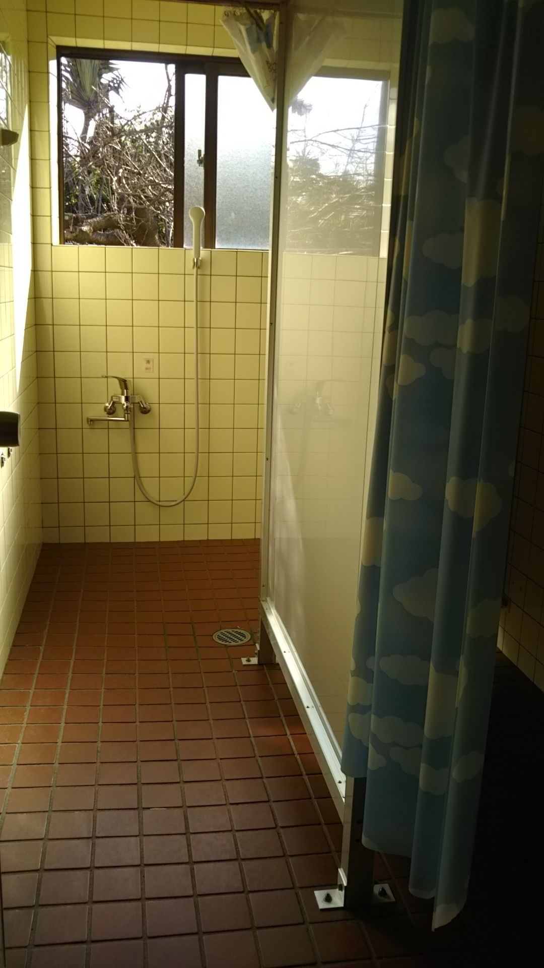 A small, tiled bathroom with a shower, a window, and a curtain.
