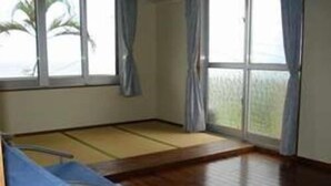 Una habitación con suelo de tatami, un sofá azul y ventanas grandes con cortinas.