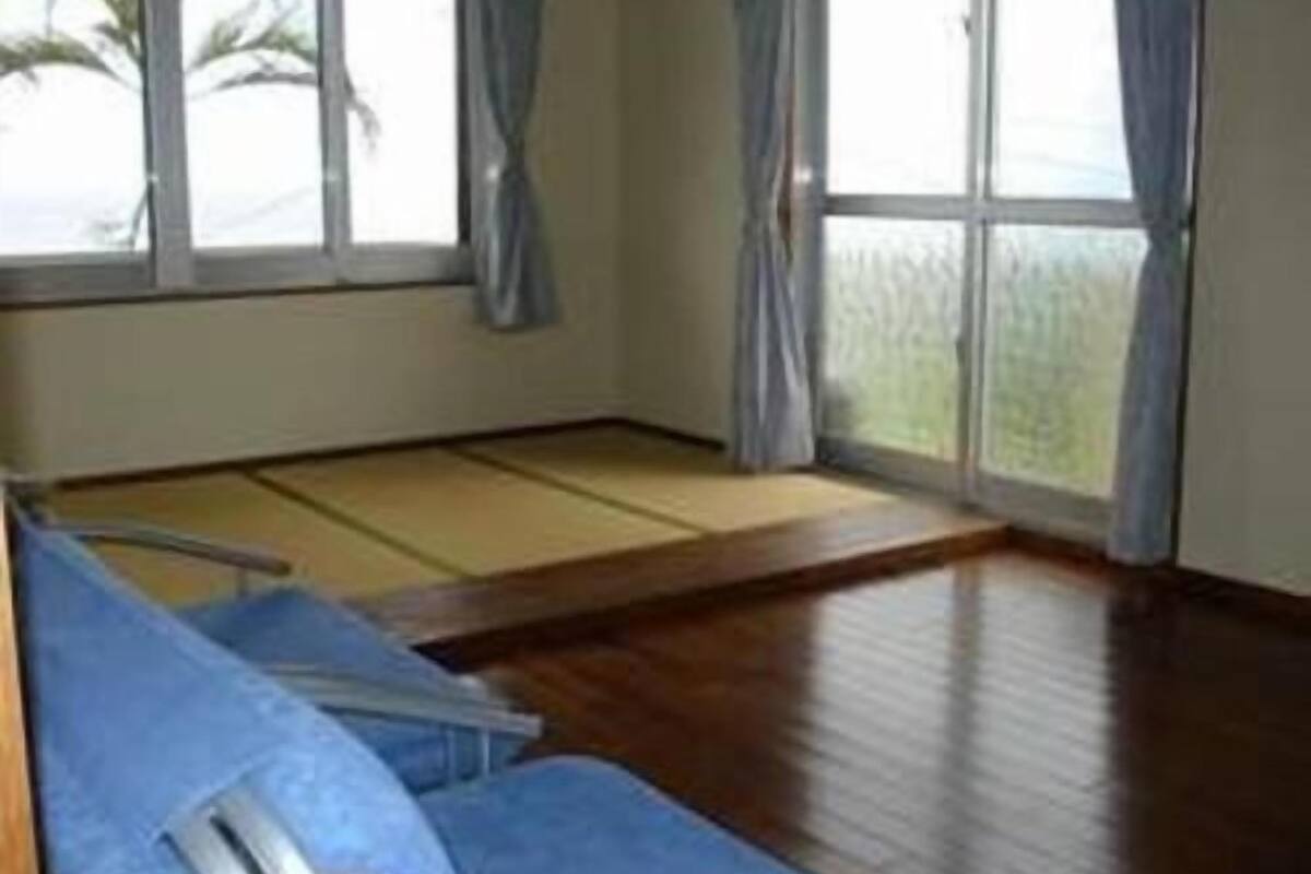 Une pièce avec un sol recouvert de tatamis, un canapé bleu et de grandes fenêtres avec des rideaux.