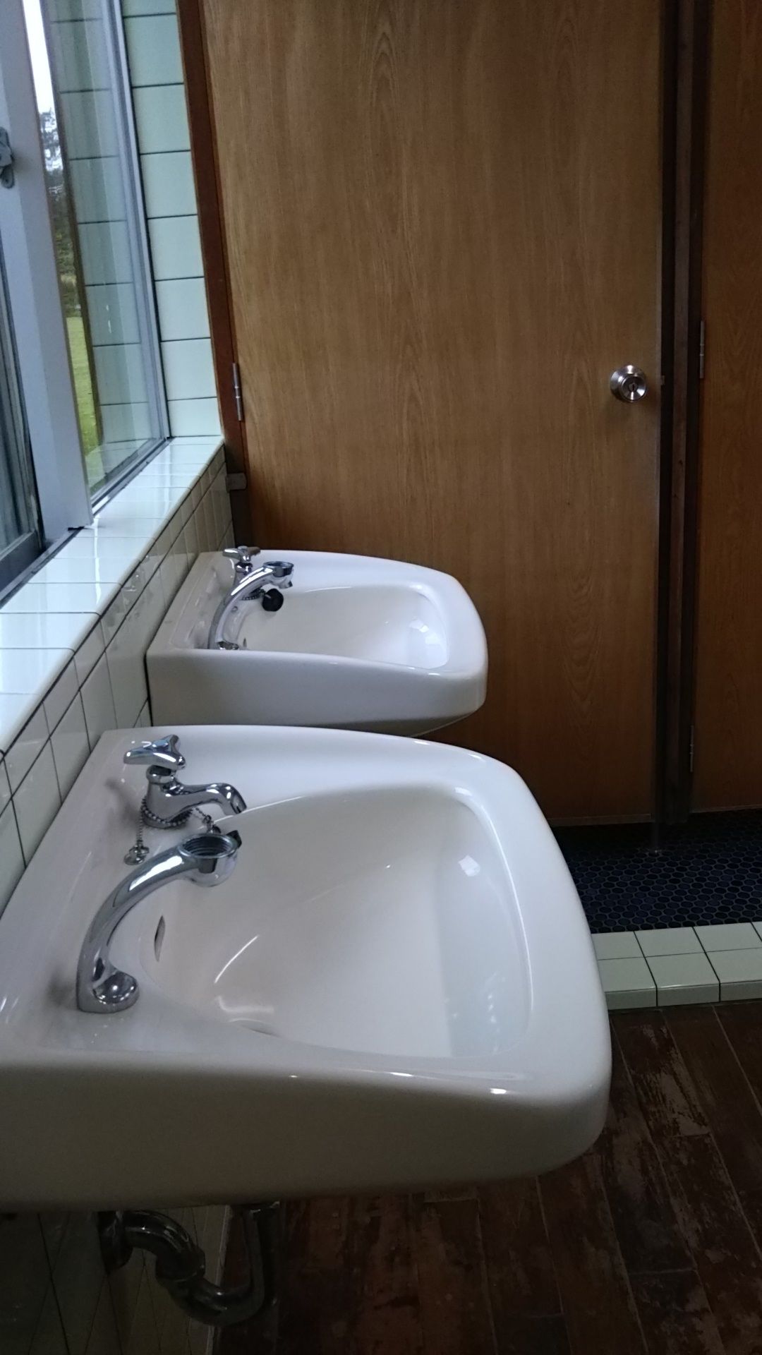 A bathroom with two sinks, a wooden door, and a tiled floor.
