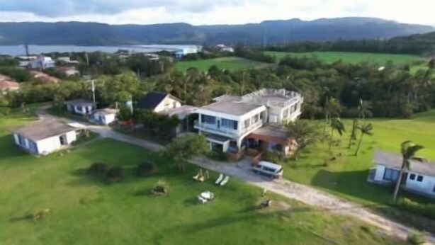 Vista aérea de una zona residencial con una casa grande que cuenta con un amplio jardín delantero, un camino de entrada y un garaje independiente pequeño.