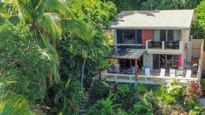 A two-story house with a balcony, surrounded by lush greenery and palm trees. - Villa Cala N°11 - 23 Steps to the Pacific Ocean, Luxury Villa with Stunning View (Bahia Pez Vela)