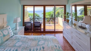 A bedroom with a bed, a nightstand, a dresser, a ceiling fan, and a sliding glass door leading to a balcony with outdoor furniture and plants. - Villa Cala N°11 - 23 Steps to the Pacific Ocean, Luxury Villa with Stunning View (Bahia Pez Vela)