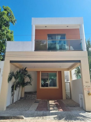 A modern two-story house with a balcony, a front entrance, and a visible address.